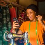 young african woman who is a tailor feeling excited and happy and jubilant while viewing content on her mobile phone